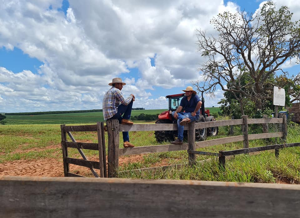 trabalhadores sentados na porteira - trator ao fundo
